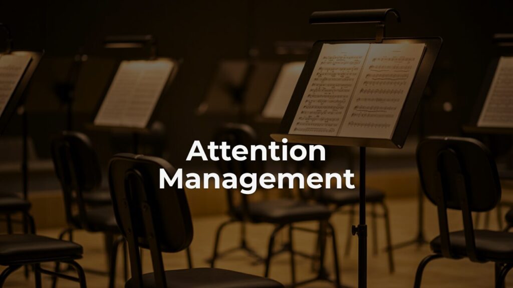 Empty orchestra chairs and music stands in warm amber light, representing attention management and the stillness between performances