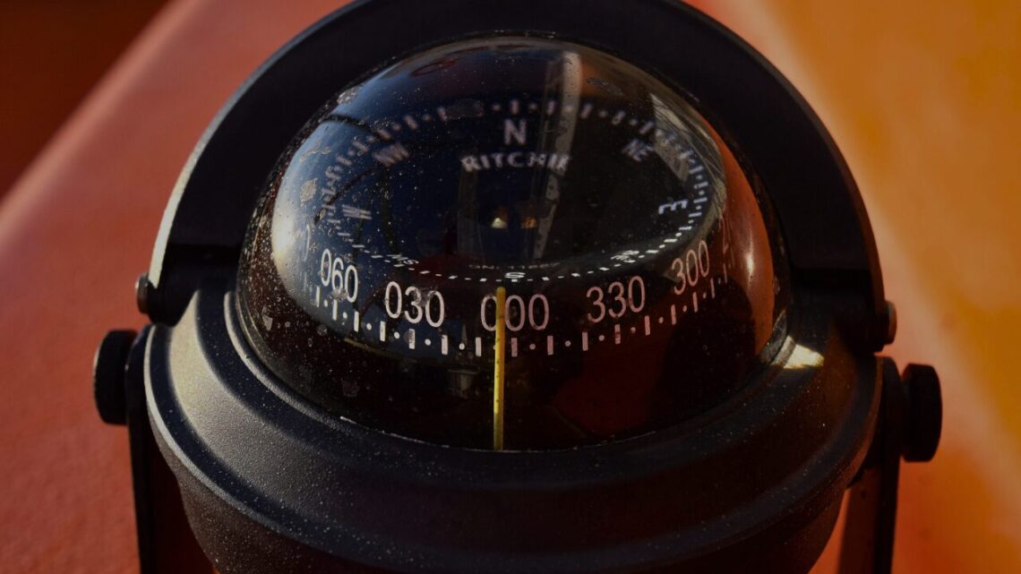 A compass resting on a weathered wooden surface in soft natural light, needle pointing steadily.