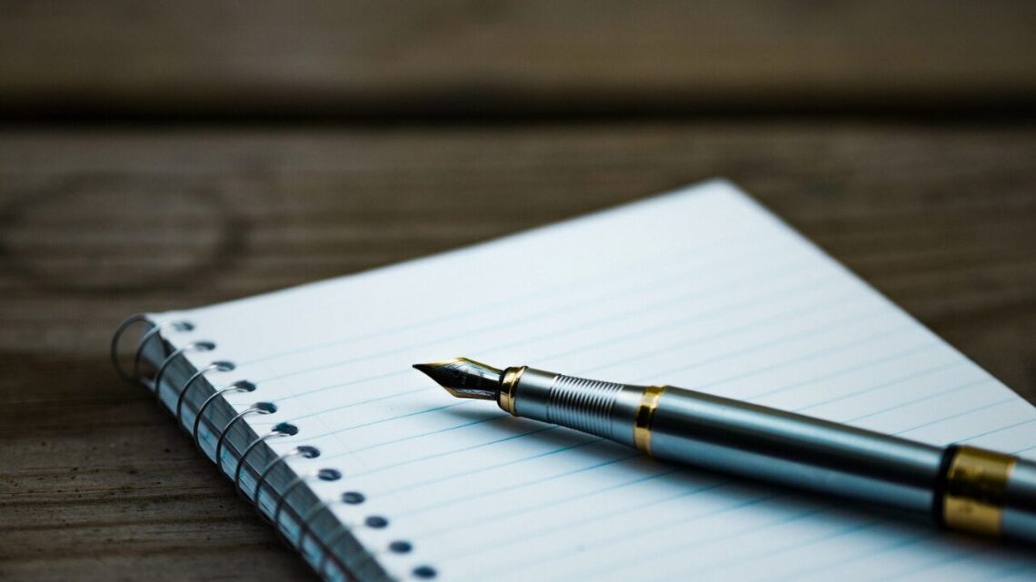 A fountain pen resting on an open notebook on a wooden desk.