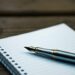 A fountain pen resting on an open notebook on a wooden desk.