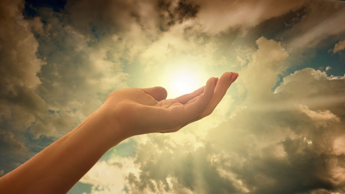 An open hand reaching gently toward sunlight through clouds