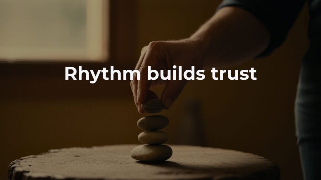 A hand carefully placing a smooth stone onto a balanced stack of four river stones resting on a worn wooden surface, in warm amber light.