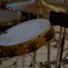 A tambourine and snare drum with drumsticks arranged in a dimly lit percussion setup, shot in close detail with shallow depth of field.