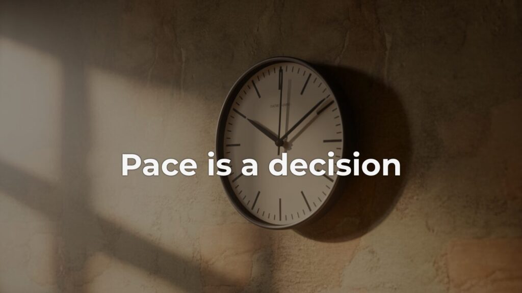 A simple analog wall clock mounted on a warm plaster wall, lit by soft diagonal window light, with the overlay text "Pace is a decision" — evoking sustainable pace as a deliberate leadership choice.