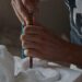 A sculptor's hands pressing a chisel into white stone, dust rising from the surface, partial figure visible in a dim workshop — the discipline of working within the properties of a medium to bring form into being.