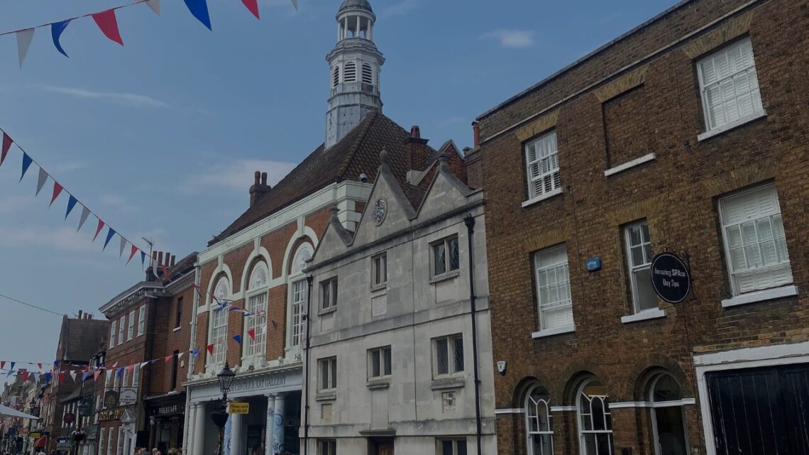 Rochester High Street in Kent, England, lined with Georgian brick buildings and red, white, and blue bunting under a bright summer sky.