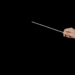 A conductor's hand holding a baton against a dark background, poised in stillness before the downbeat.