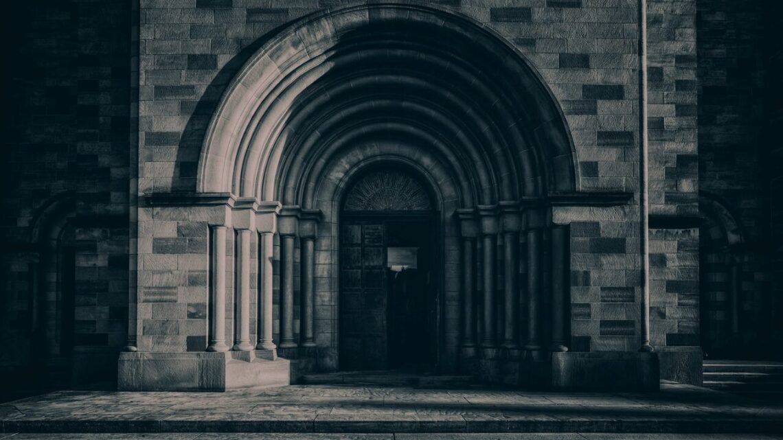 The Romanesque stone archway of a historic building, its layered concentric arch framing a darkened entrance, rendered in deep cool tones — a threshold held open, waiting.