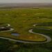 Aerial view of a winding river bend tracing its path upstream through green wetland terrain.