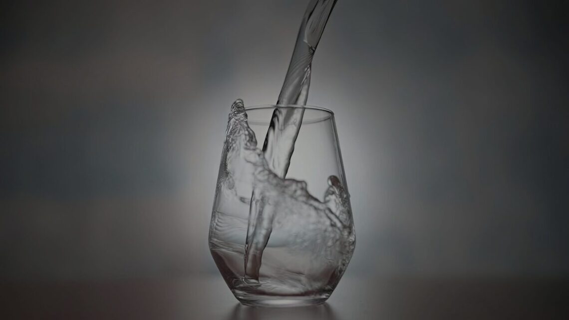 Water pouring into a clear glass, capturing a mid-splash moment against a softly lit, dark background.