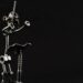 A miniature handcrafted sculpture of a conductor, made from nuts, bolts, and scrap metal, baton raised mid-gesture against a plain black background
