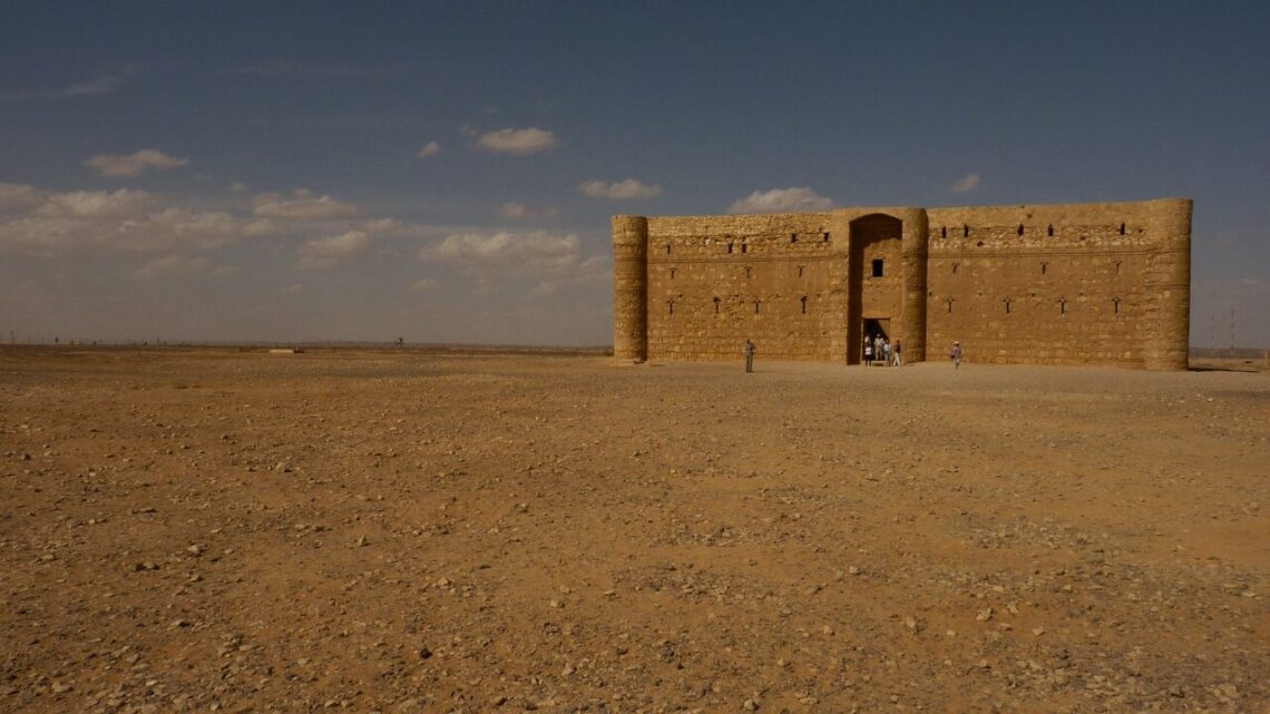 An ancient stone fort standing alone on a vast desert plain under a wide blue sky with scattered clouds.