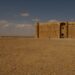An ancient stone fort standing alone on a vast desert plain under a wide blue sky with scattered clouds.