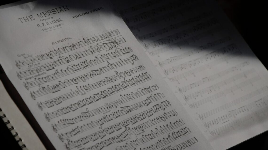 Sunlight falling across an open score of Handel's Messiah, violin part, resting on a spiral-bound notebook.