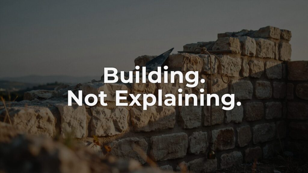 An unfinished stone wall at dusk with a trowel and rope left mid-task, embodying the quiet authority of staying with the work instead of the argument.