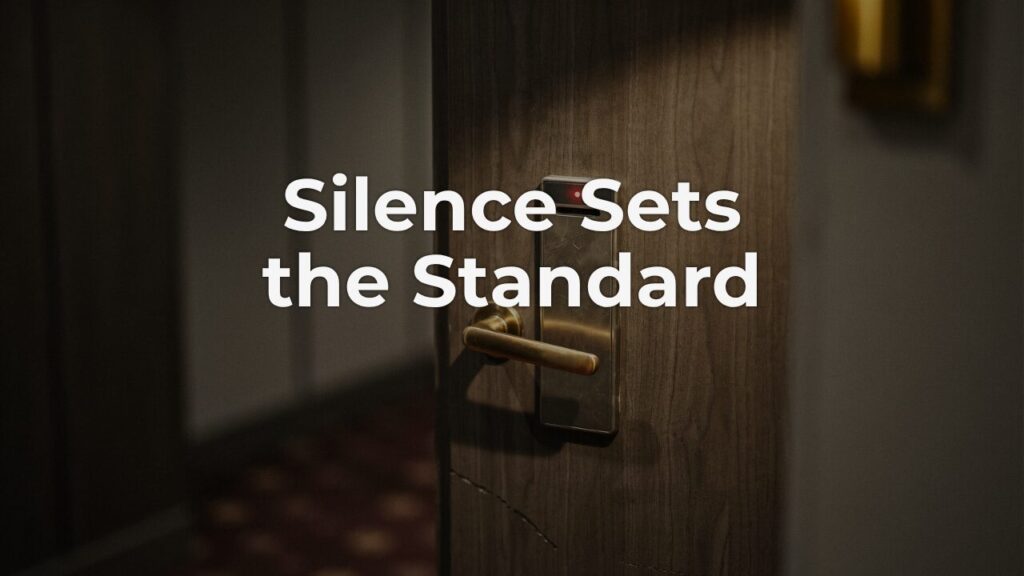 A weathered hotel room door with a brass handle and a small red light blinking on the keycard lock, a quiet reminder of what you tolerate going unfixed.