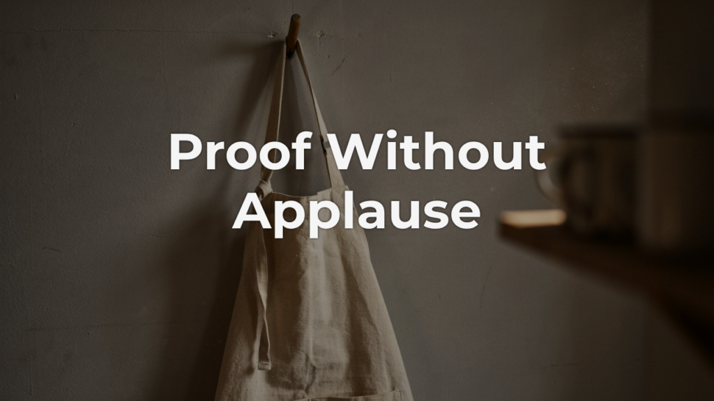 ALT text: A faded canvas work apron hangs from a simple wooden hook, the fabric worn soft at the ties from years of the same quiet repetition — the kind of trust nobody had to announce.