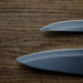 Two kitchen knives rest on a deeply worn wooden cutting board, its surface etched with years of the same daily strokes.