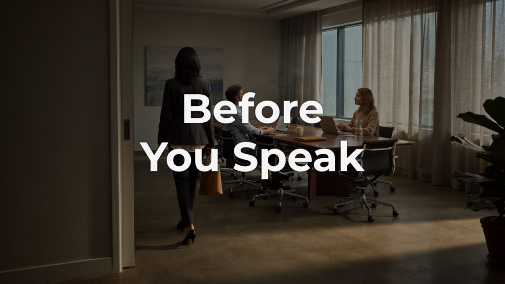 A woman walks into a sunlit conference room as two colleagues at the table look up, capturing a leader's presence entering a room before a word is spoken.