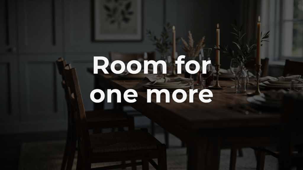 A wooden dining chair pulled up to the end of a candlelit table set for a shared meal, showing excellence as care in the extra place made ready.