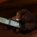 A hand holding a phone with a messaging app open, thumb hovering over the keyboard in dim light, a late-night message about to be sent.